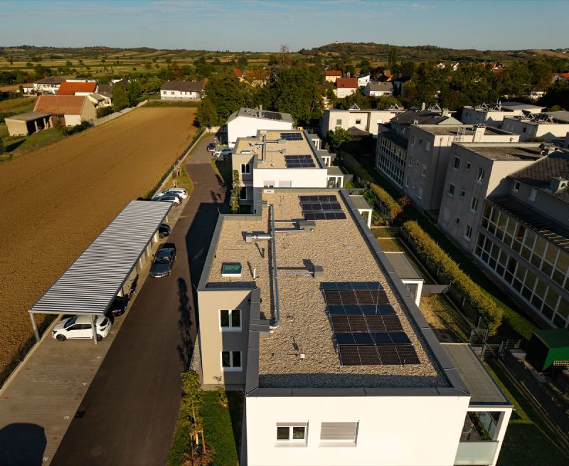 Flachdach eines Wohnhauses mit Photovoltaik, daneben die Carports der Anlage